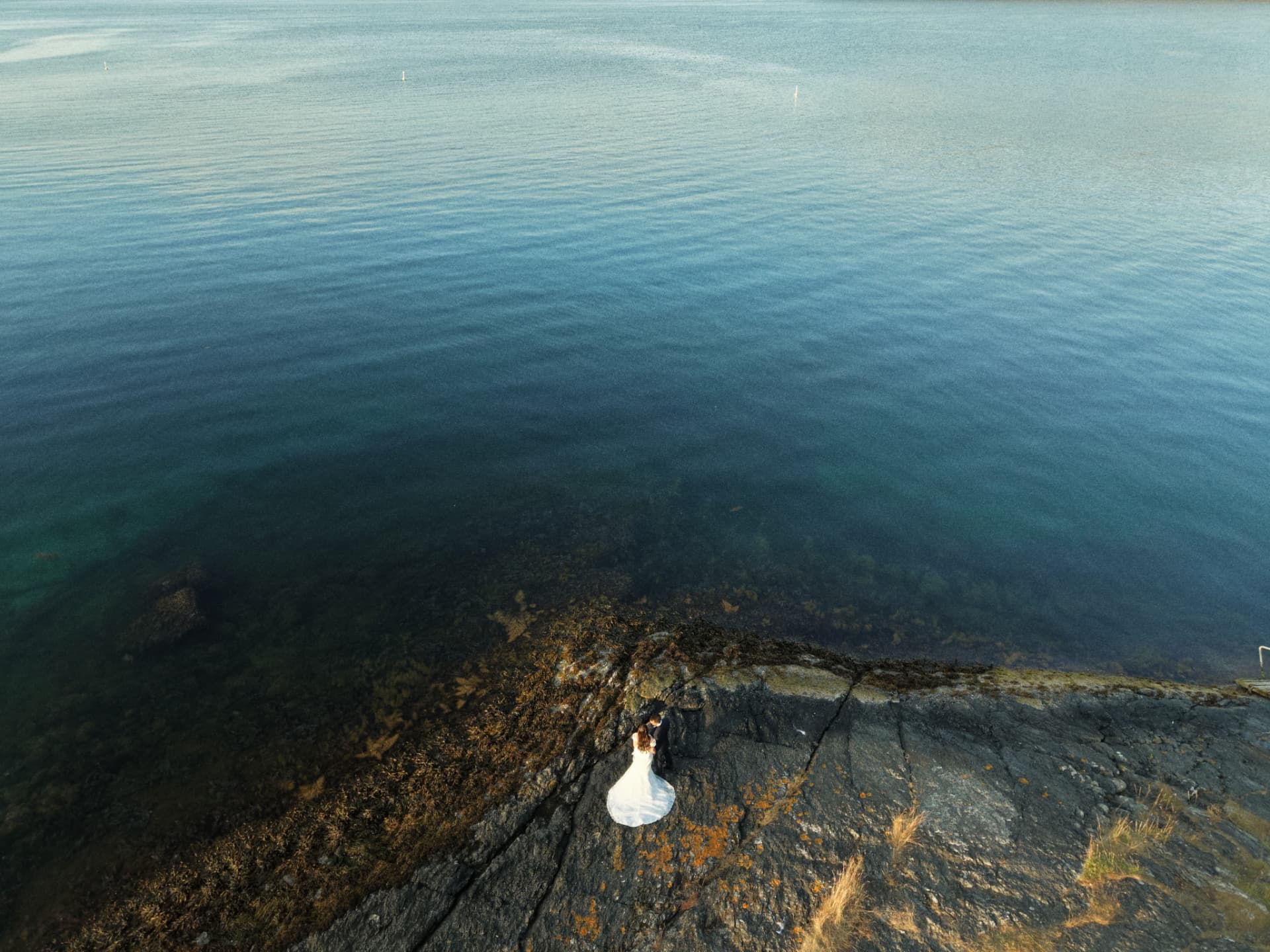 Aerial view of the couple embracing on the rocks above the water