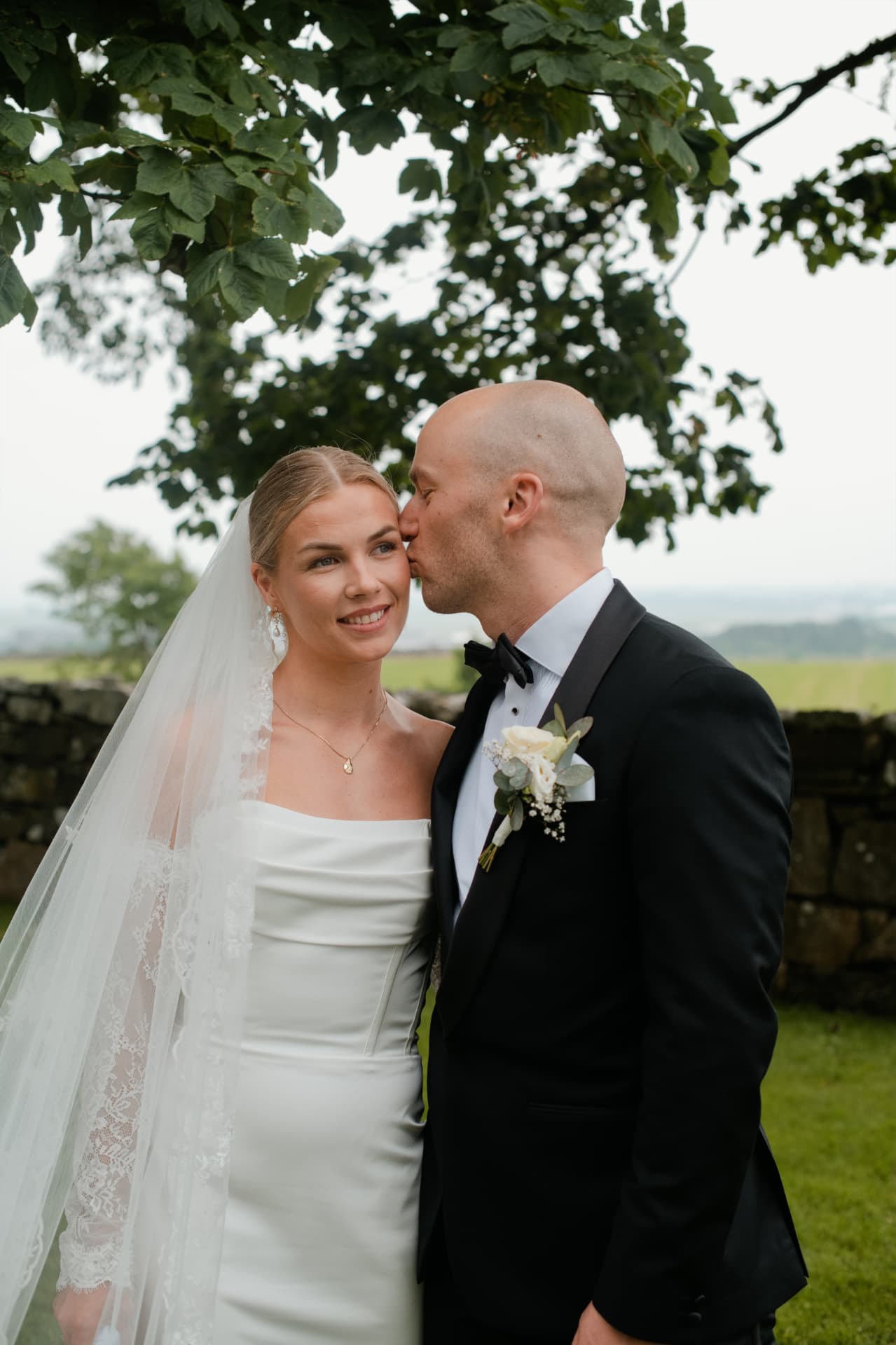 Groom kissing his bride beneath a tree