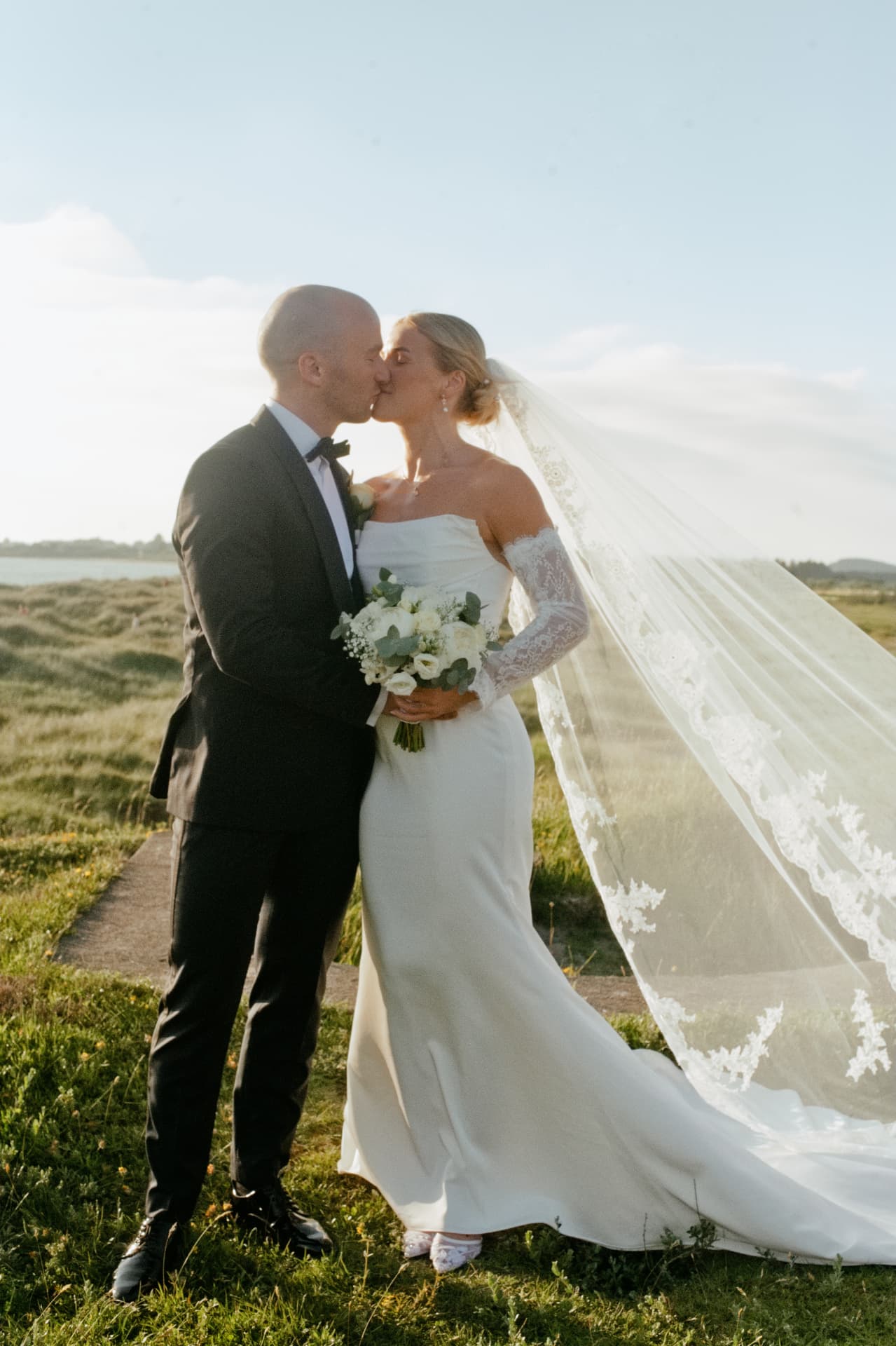 Couple kissing with the veil trailing in the evening light