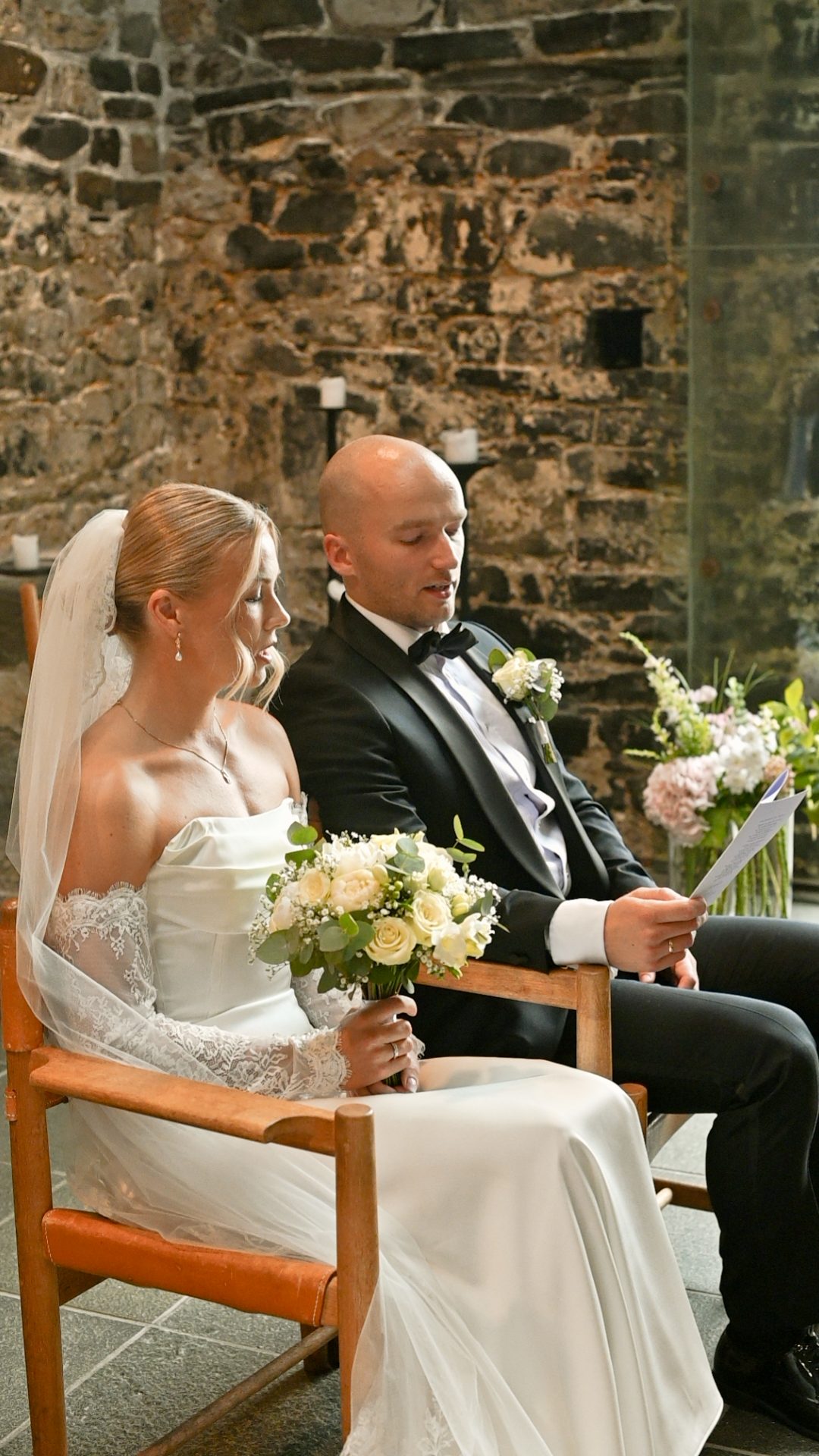 Bride and groom seated during the ceremony in a stone church