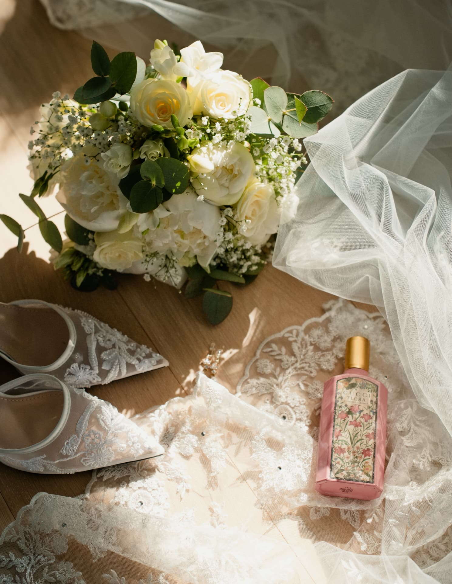 Bridal shoes, bouquet and perfume resting on lace in the morning light